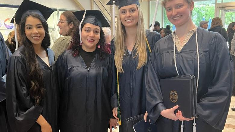 Four graduates wearing caps and gowns pose for picture at a graduation ceremony